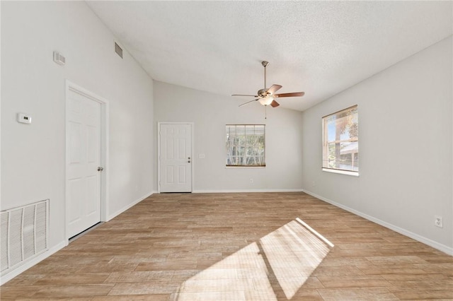 empty room with a textured ceiling, light wood-type flooring, ceiling fan, and lofted ceiling