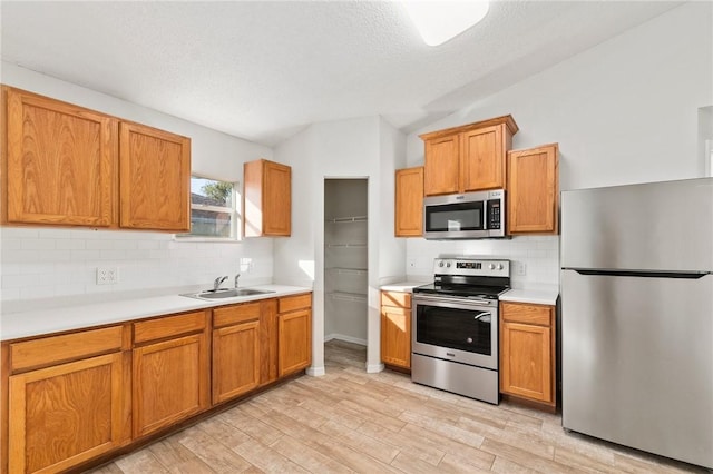 kitchen featuring sink, lofted ceiling, stainless steel appliances, and light hardwood / wood-style flooring