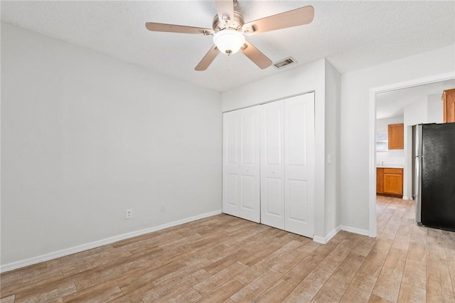 unfurnished bedroom featuring a textured ceiling, ceiling fan, light hardwood / wood-style flooring, stainless steel refrigerator, and a closet