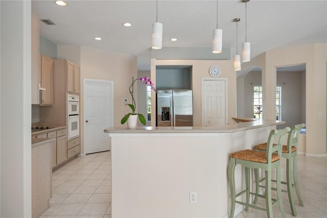 kitchen with a kitchen island with sink, light brown cabinets, stainless steel fridge, and light tile patterned floors