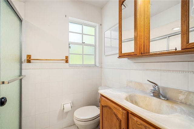 bathroom featuring a shower with door, vanity, toilet, and tile walls