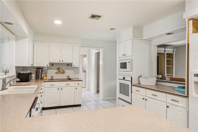 kitchen with light tile patterned flooring, white cabinetry, backsplash, sink, and white appliances