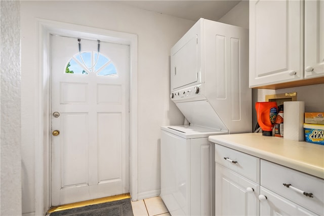 clothes washing area featuring cabinets, light tile patterned flooring, and stacked washer and clothes dryer