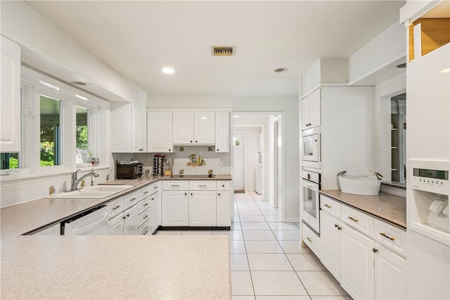 kitchen with white cabinetry, backsplash, light tile patterned floors, sink, and white appliances