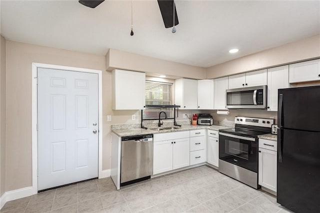 kitchen featuring light stone counters, appliances with stainless steel finishes, white cabinets, a sink, and baseboards