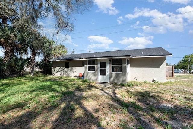 rear view of house with roof with shingles, a lawn, and stucco siding