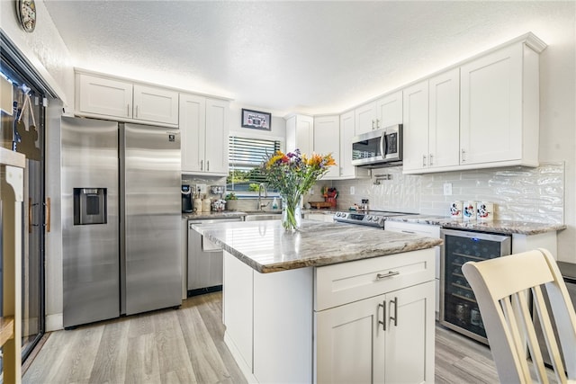 kitchen featuring wine cooler, a center island, appliances with stainless steel finishes, and white cabinets