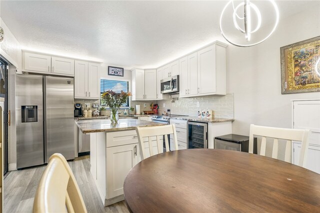 kitchen featuring stainless steel appliances, white cabinetry, decorative light fixtures, and light hardwood / wood-style flooring