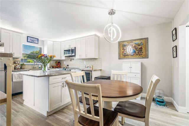 kitchen with white cabinetry, light hardwood / wood-style floors, hanging light fixtures, and dark stone countertops