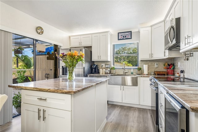 kitchen featuring light stone counters, a kitchen island, appliances with stainless steel finishes, sink, and white cabinets