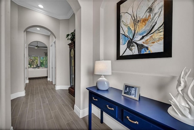 hallway with arched walkways, baseboards, wood tiled floor, crown molding, and recessed lighting