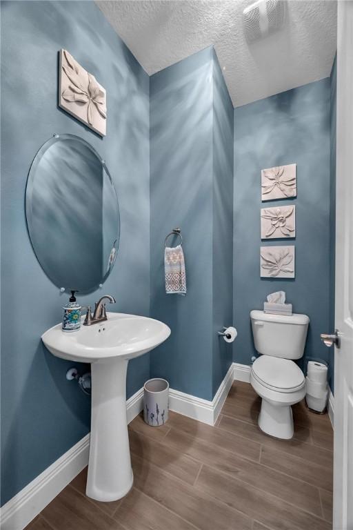 half bathroom with toilet, a textured ceiling, baseboards, and wood finished floors