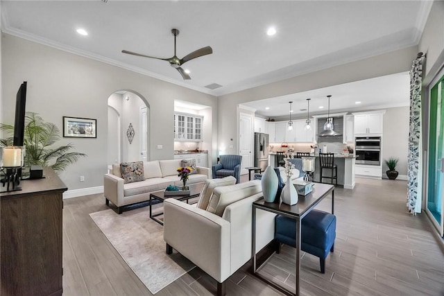 living room featuring arched walkways, light wood finished floors, baseboards, and crown molding