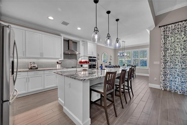 kitchen featuring wall chimney range hood, appliances with stainless steel finishes, crown molding, and wood finished floors