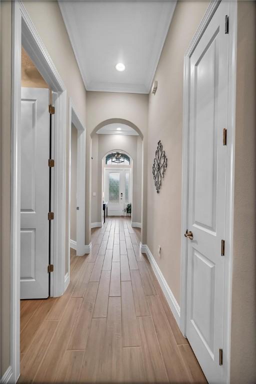 hall with baseboards, arched walkways, ornamental molding, and wood finish floors