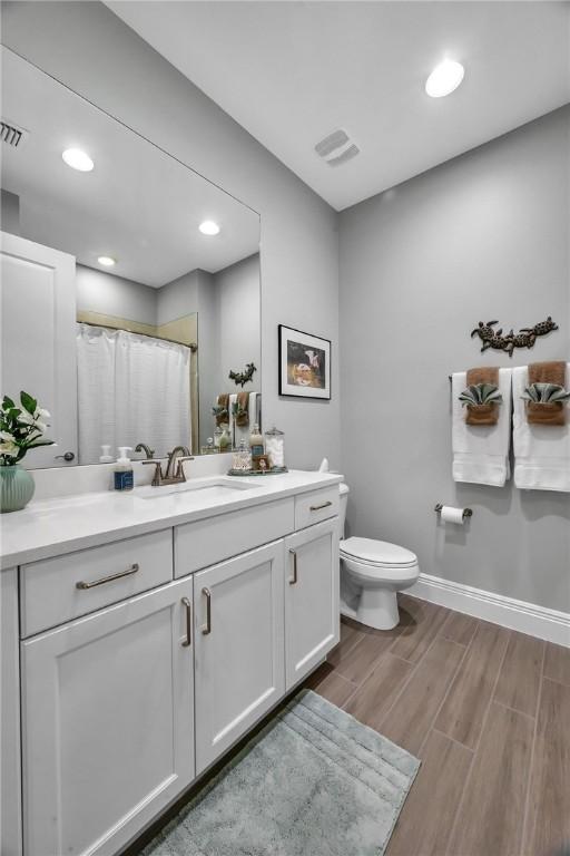 bathroom with toilet, wood finished floors, vanity, visible vents, and baseboards