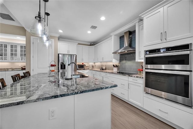 kitchen with stainless steel appliances, backsplash, white cabinetry, a sink, and wall chimney exhaust hood