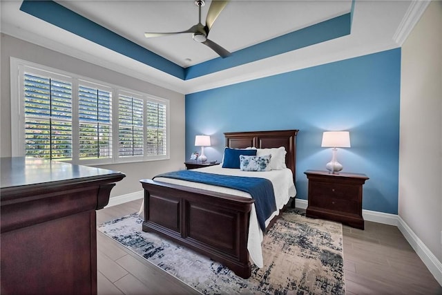 bedroom with a ceiling fan, baseboards, a raised ceiling, and wood finished floors