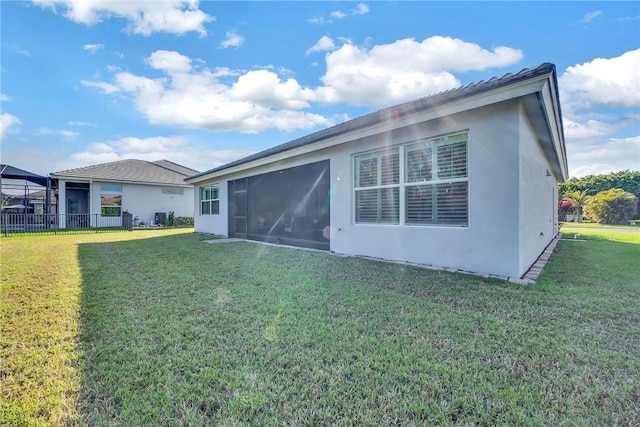 rear view of house with stucco siding, a sunroom, and a yard