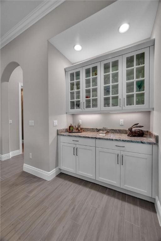 bar with arched walkways, baseboards, light wood-style flooring, ornamental molding, and a bar