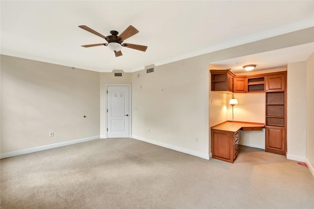 unfurnished room featuring ceiling fan, light colored carpet, built in desk, and ornamental molding