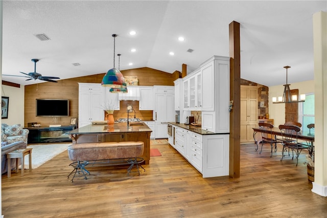 kitchen with lofted ceiling, a center island with sink, white cabinets, hanging light fixtures, and light hardwood / wood-style flooring