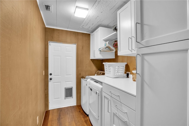 laundry area featuring cabinets, wood-type flooring, wood walls, and independent washer and dryer