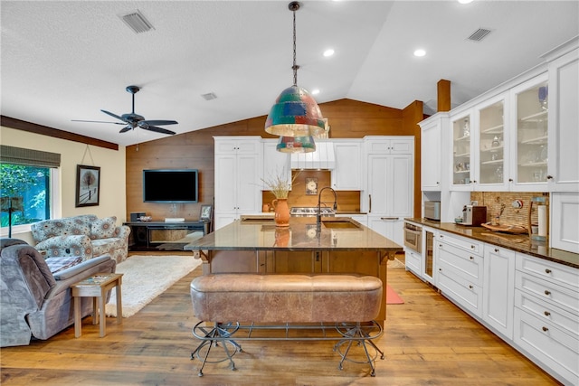 kitchen featuring light hardwood / wood-style floors, a center island with sink, a kitchen breakfast bar, lofted ceiling, and pendant lighting