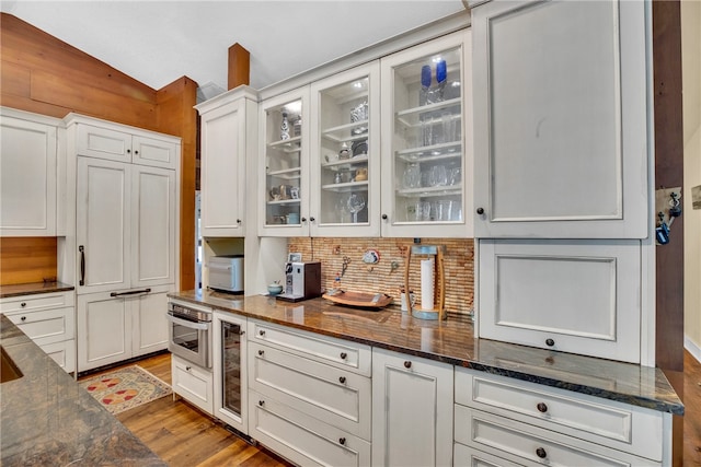 kitchen with white cabinetry, light hardwood / wood-style floors, lofted ceiling, and dark stone countertops