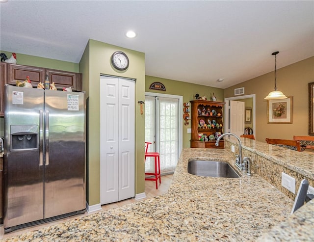 kitchen with vaulted ceiling, hanging light fixtures, sink, light stone countertops, and stainless steel fridge