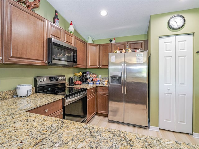 kitchen featuring stainless steel appliances, light stone countertops, vaulted ceiling, and light hardwood / wood-style floors