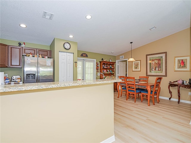 kitchen with light stone counters, light wood-type flooring, pendant lighting, stainless steel refrigerator with ice dispenser, and vaulted ceiling