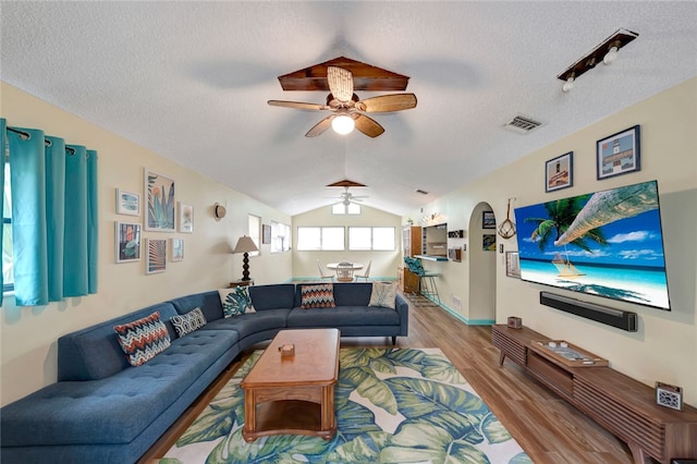 living room featuring a textured ceiling, vaulted ceiling, ceiling fan, and light hardwood / wood-style flooring