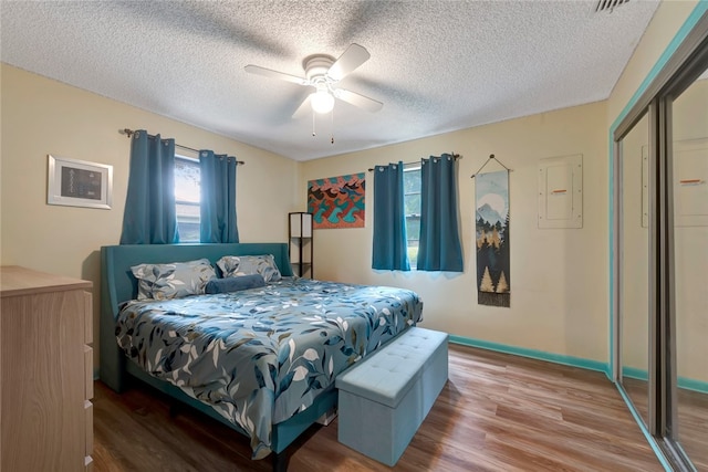 bedroom featuring electric panel, wood-type flooring, a textured ceiling, ceiling fan, and a closet