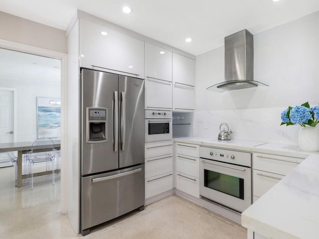 kitchen featuring white cabinetry, wall chimney range hood, white appliances, and light stone countertops