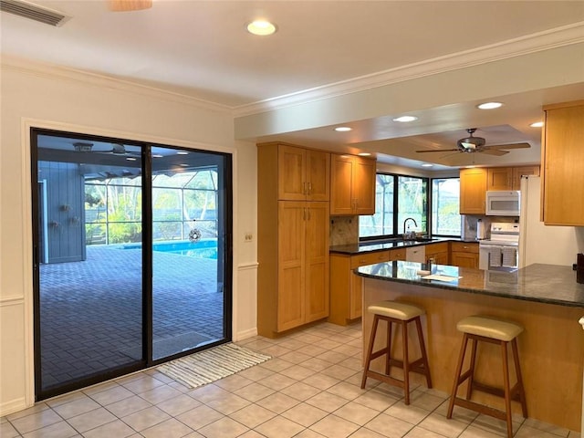 675 Colonial Dr, Vero Beach, FL 32962 - kitchen with white appliances, a peninsula, ornamental molding, a breakfast bar area, and light tile patterned floors