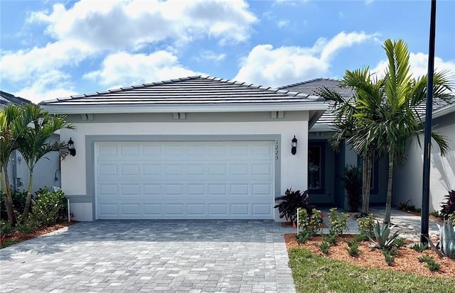 view of front of home with a tile roof, decorative driveway, an attached garage, and stucco siding