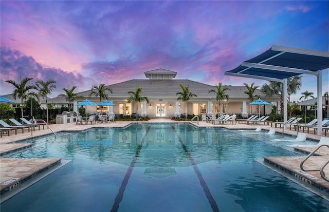 pool at dusk with a patio, a community pool, and fence