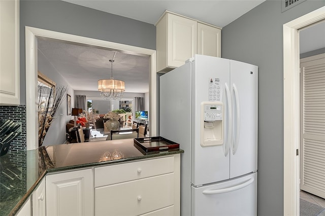 kitchen with white cabinetry, hanging light fixtures, tasteful backsplash, white refrigerator with ice dispenser, and a notable chandelier