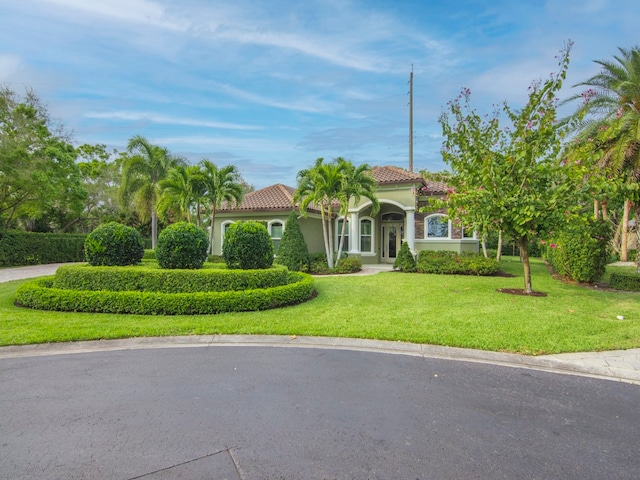 mediterranean / spanish home featuring a front yard, a tiled roof, and stucco siding