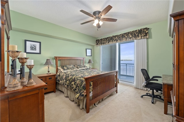 carpeted bedroom featuring access to exterior, a water view, a textured ceiling, and ceiling fan