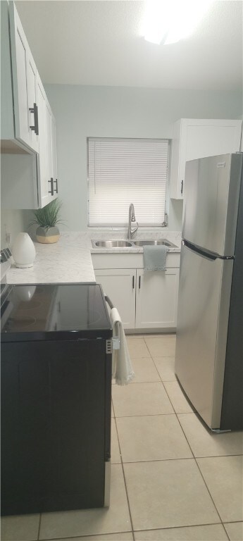 kitchen with electric range oven, light tile patterned flooring, freestanding refrigerator, and white cabinetry