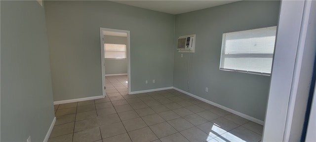 spare room featuring light tile patterned flooring, baseboards, and a wall mounted air conditioner