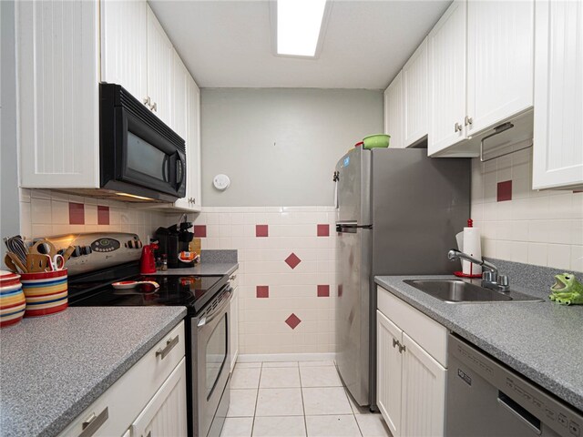 kitchen featuring stainless steel appliances, tile walls, light tile patterned floors, sink, and white cabinetry