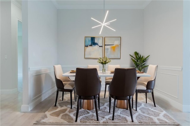 dining space featuring light wood-type flooring, ornamental molding, a chandelier, and a decorative wall