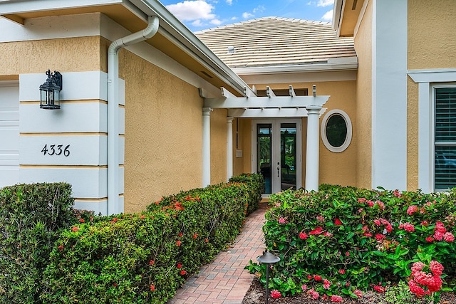 entrance to property with stucco siding, french doors, a tile roof, and a garage