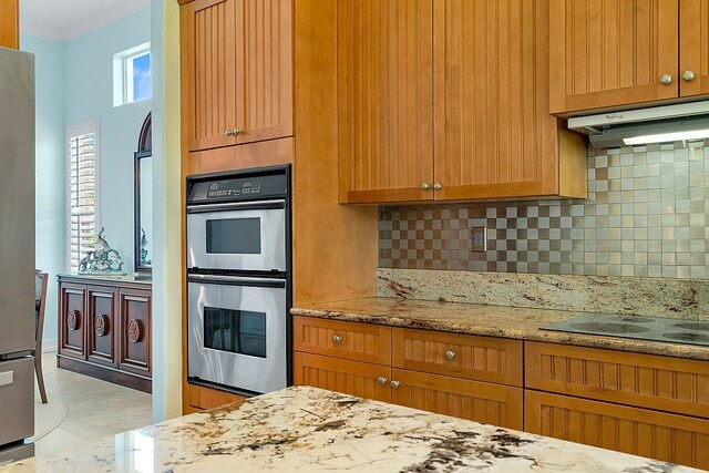 kitchen with light tile patterned flooring, backsplash, light stone countertops, double oven, and electric cooktop