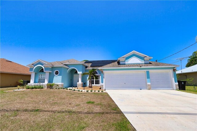 6029 Winfield Dr, Port St Lucie, FL 34986 - view of front of house featuring a front lawn, stone siding, concrete driveway, an attached garage, and solar panels