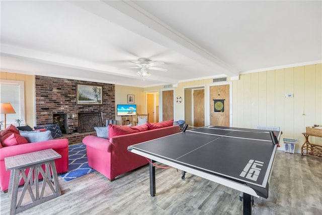 playroom with wood walls, ceiling fan, beam ceiling, a fireplace, and wood-type flooring