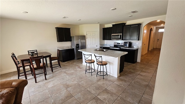 kitchen featuring a center island with sink, sink, appliances with stainless steel finishes, a kitchen breakfast bar, and a textured ceiling